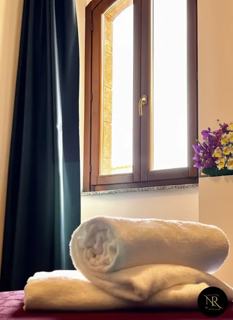 Rolled white towels on a bed by the wooden window of a room in central Viterbo