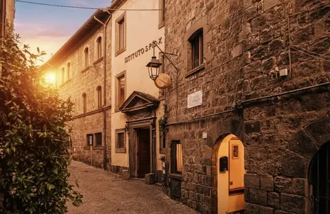 Via San Tommaso at sunset: the stone alley and historic entrance of Istituto San Pio X, home of Nazareth Residence in Viterbo