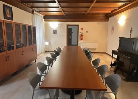 Room with a twelve-seat long table, upright piano and coffered ceiling, for events in Viterbo