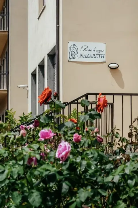 The Residenza Nazareth sign on the Via San Tommaso facade, among the garden roses