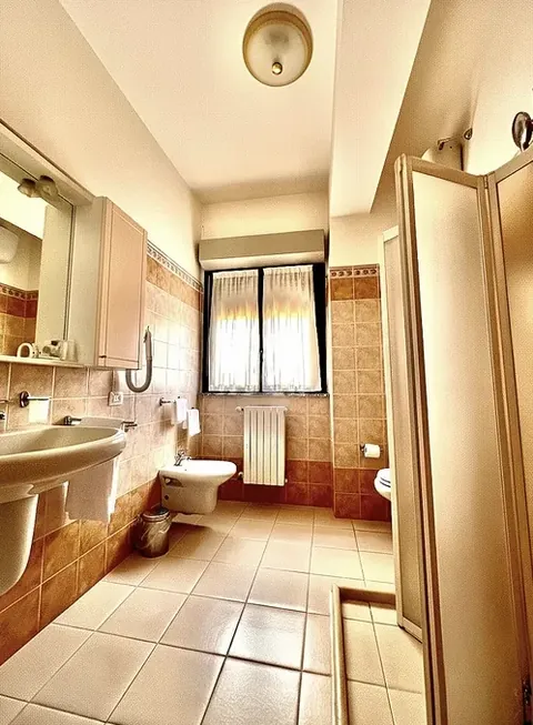 Bathroom with shower cubicle, bidet and curtained window, tiled in warm terracotta tones