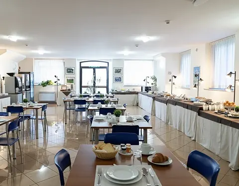 Bright breakfast room with buffet, laid tables and blue chairs, for groups of up to 100 in Viterbo